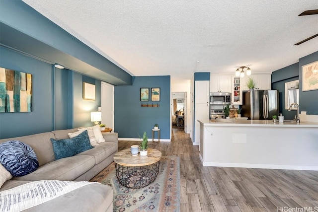 living room with a ceiling fan, a textured ceiling, baseboards, and wood finished floors