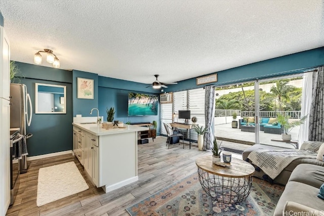 living area featuring a textured ceiling, ceiling fan, light wood-style flooring, and baseboards