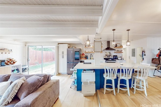 kitchen with pendant lighting, wall chimney range hood, appliances with stainless steel finishes, a kitchen breakfast bar, and a kitchen island