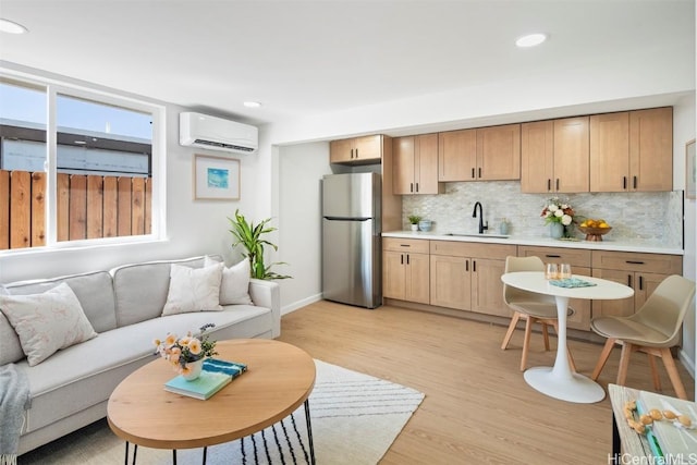 kitchen featuring sink, light wood-type flooring, an AC wall unit, stainless steel fridge, and decorative backsplash