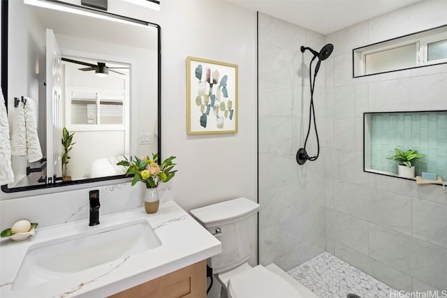 bathroom featuring vanity, a tile shower, ceiling fan, and toilet