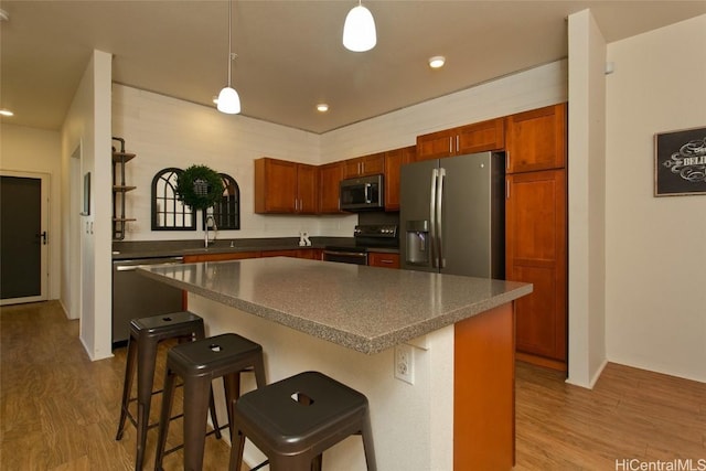 kitchen featuring hanging light fixtures, appliances with stainless steel finishes, a center island, and a kitchen bar