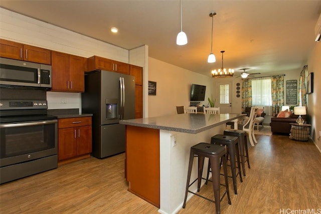 kitchen with appliances with stainless steel finishes, a kitchen bar, a center island, and light hardwood / wood-style flooring