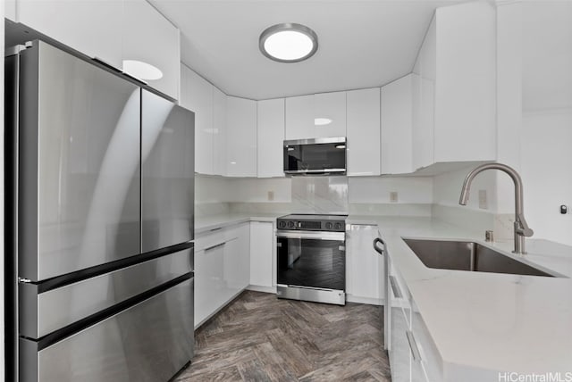 kitchen with sink, white cabinetry, stainless steel appliances, light stone counters, and dark parquet flooring