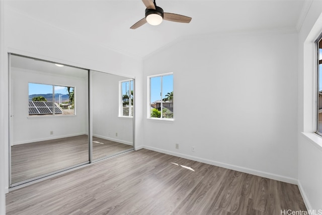 unfurnished bedroom featuring multiple windows, ornamental molding, a closet, and light wood-type flooring