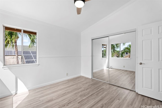 unfurnished bedroom with multiple windows, vaulted ceiling, a closet, and light wood-type flooring