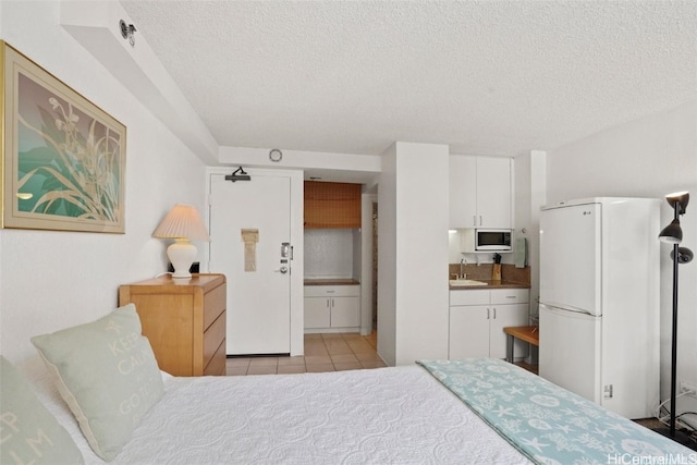 tiled bedroom featuring white refrigerator, ensuite bathroom, sink, and a textured ceiling