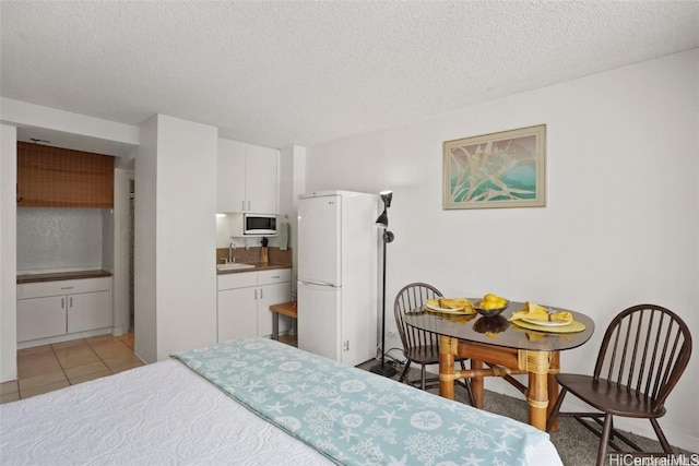 bedroom featuring ensuite bathroom, sink, white fridge, light tile patterned floors, and a textured ceiling