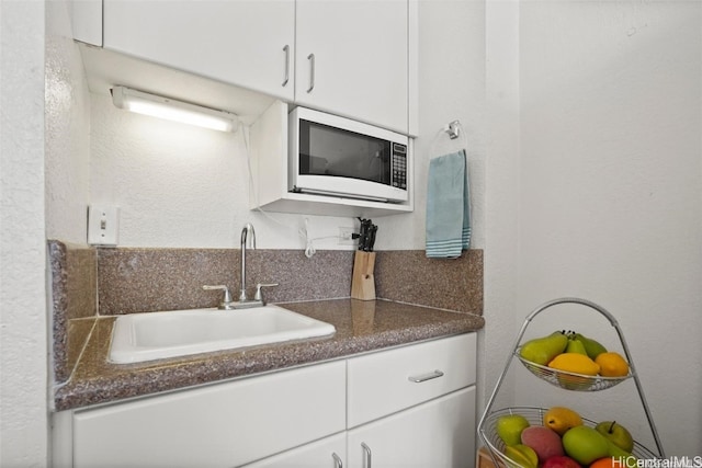 kitchen featuring sink, white microwave, and white cabinets