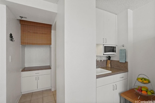 kitchen featuring built in microwave, sink, white cabinetry, a textured ceiling, and light tile patterned floors