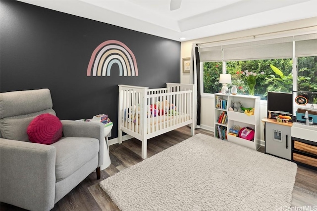 bedroom with a crib, dark wood-type flooring, and ceiling fan