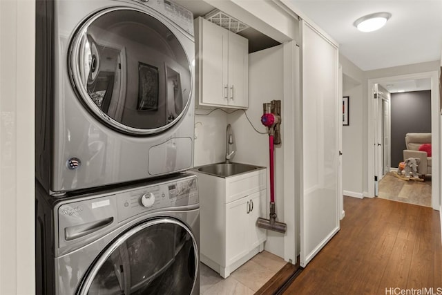 laundry room featuring sink, light hardwood / wood-style flooring, cabinets, and stacked washer / dryer