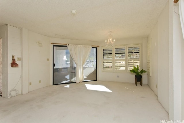 empty room with a textured ceiling, light colored carpet, and a chandelier