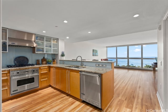 kitchen featuring sink, kitchen peninsula, stainless steel appliances, a water view, and wall chimney exhaust hood