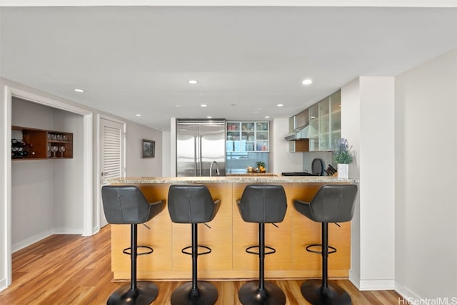 kitchen featuring a kitchen bar, white cabinetry, built in refrigerator, kitchen peninsula, and light hardwood / wood-style floors