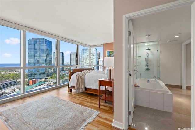 bedroom with a city view, wood finished floors, floor to ceiling windows, and ensuite bathroom