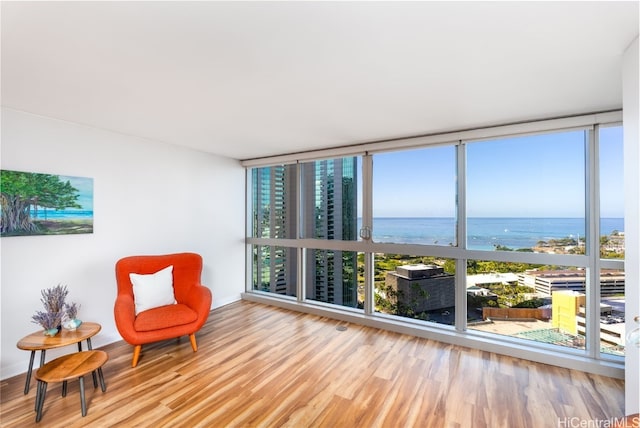 sitting room featuring a water view, light wood-type flooring, and a wall of windows