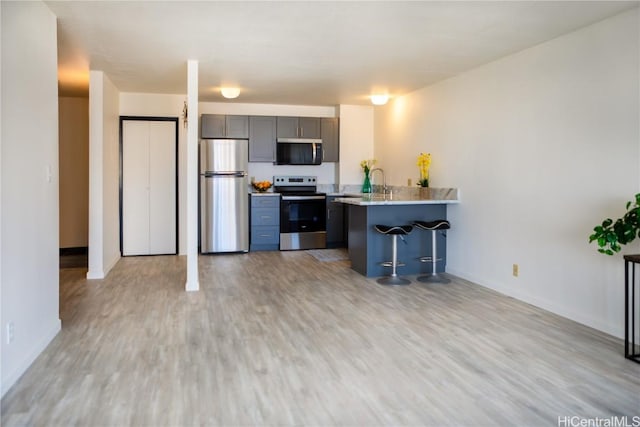 kitchen featuring stainless steel appliances, a breakfast bar, light hardwood / wood-style floors, and kitchen peninsula