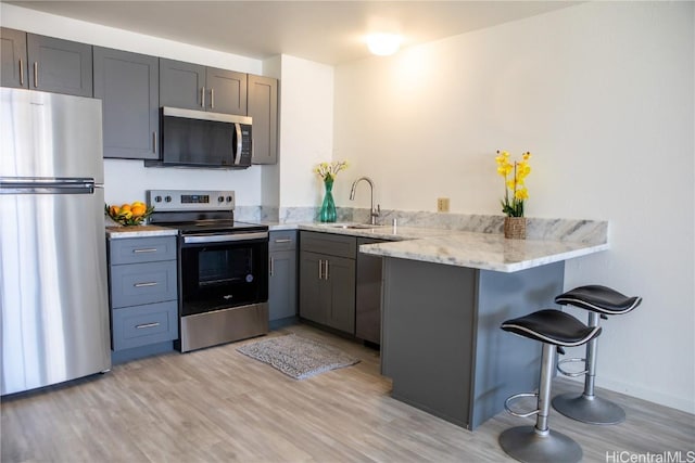 kitchen with sink, a kitchen bar, light hardwood / wood-style floors, kitchen peninsula, and stainless steel appliances