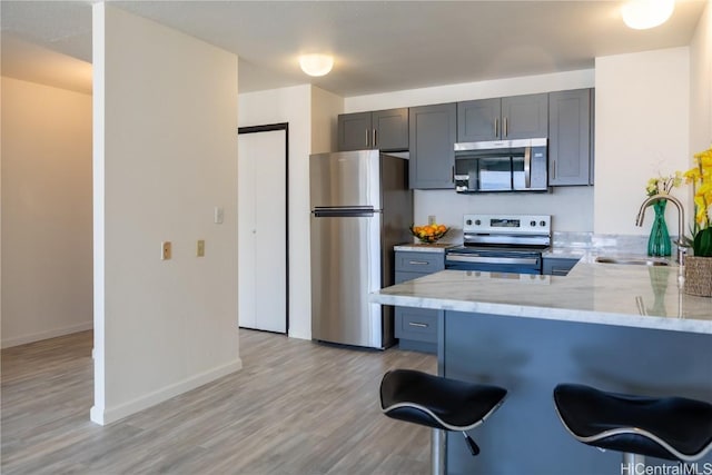 kitchen with sink, a breakfast bar area, light stone counters, appliances with stainless steel finishes, and kitchen peninsula