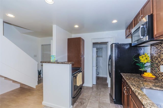 kitchen featuring tasteful backsplash, appliances with stainless steel finishes, dark stone countertops, and kitchen peninsula