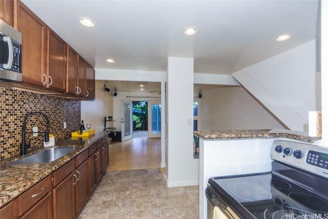 kitchen featuring sink, appliances with stainless steel finishes, dark stone countertops, decorative backsplash, and kitchen peninsula