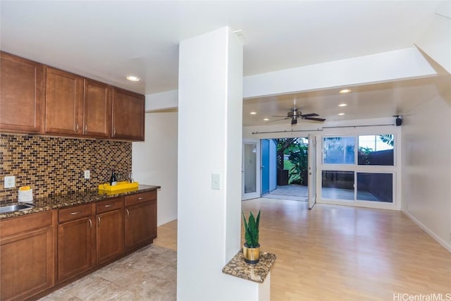 kitchen featuring sink, tasteful backsplash, light hardwood / wood-style flooring, dark stone countertops, and ceiling fan