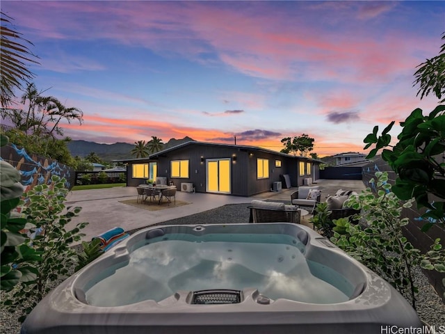 pool at dusk with a hot tub, a mountain view, and a patio area