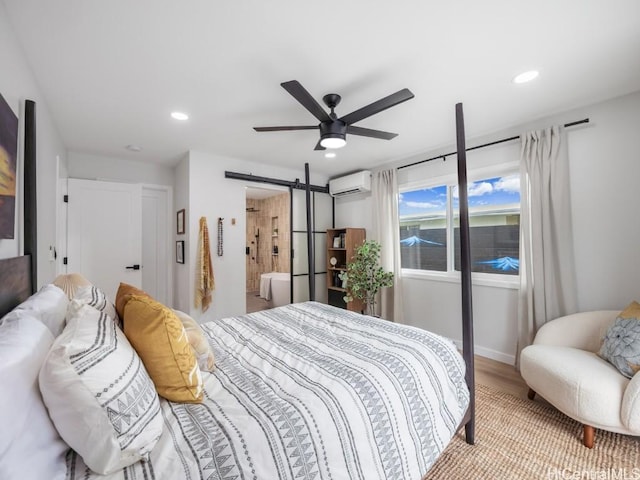 bedroom featuring a wall mounted air conditioner, hardwood / wood-style flooring, a barn door, and ceiling fan