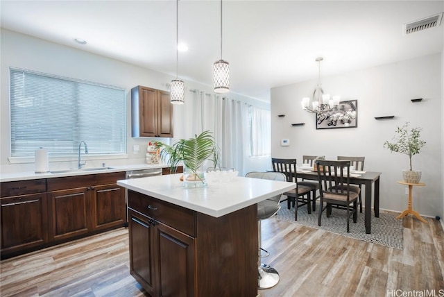 kitchen with a kitchen bar, sink, decorative light fixtures, a kitchen island, and light hardwood / wood-style floors