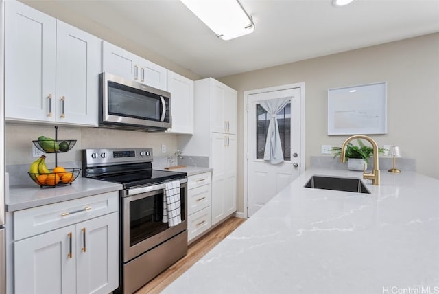 kitchen with a sink, white cabinets, appliances with stainless steel finishes, light stone countertops, and light wood finished floors