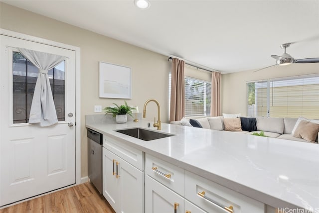 kitchen with a sink, light wood-style floors, white cabinets, light countertops, and dishwasher