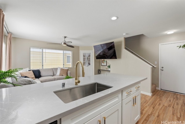 kitchen featuring white cabinets, ceiling fan, open floor plan, light wood-type flooring, and a sink