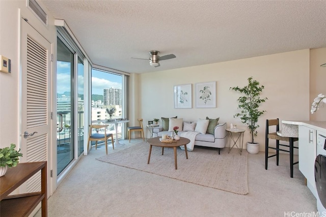 living room featuring ceiling fan, floor to ceiling windows, a textured ceiling, washer / dryer, and light colored carpet