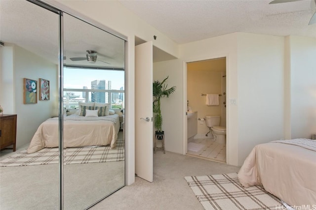 carpeted bedroom with a textured ceiling, a closet, ceiling fan, and ensuite bathroom