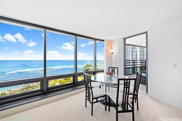 carpeted dining space with a view of the beach, a wall of windows, and a water view