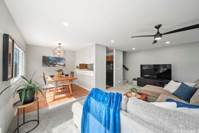 living room with ceiling fan with notable chandelier and light hardwood / wood-style flooring