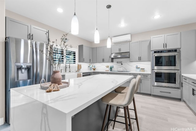 kitchen with light stone counters, a wall mounted AC, hanging light fixtures, appliances with stainless steel finishes, and a kitchen island