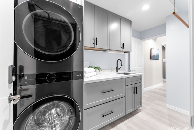 washroom featuring cabinets, stacked washer and clothes dryer, sink, and light hardwood / wood-style floors