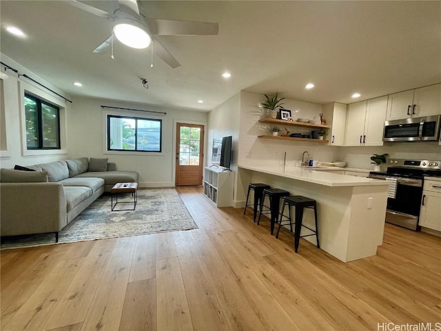 kitchen with appliances with stainless steel finishes, a breakfast bar area, white cabinets, kitchen peninsula, and light wood-type flooring