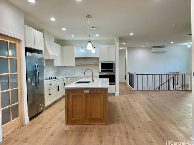 kitchen featuring pendant lighting, white cabinetry, a kitchen island with sink, stainless steel refrigerator with ice dispenser, and custom range hood