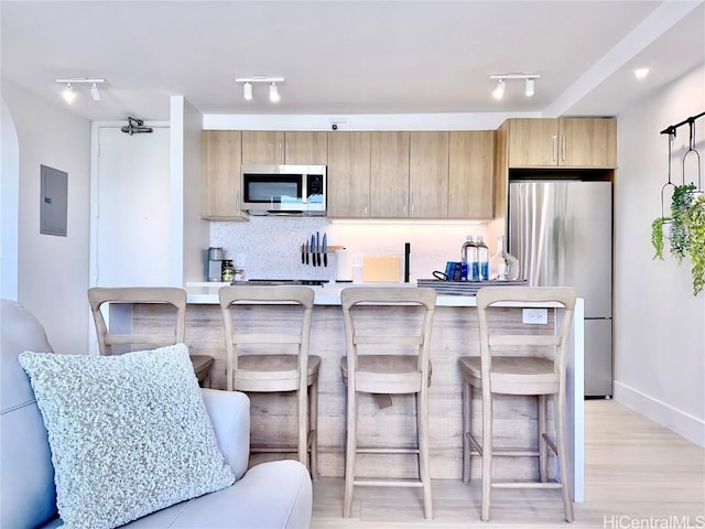 kitchen featuring stainless steel appliances, a breakfast bar area, electric panel, and backsplash