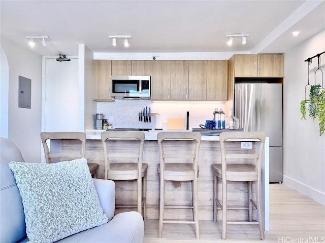 kitchen with appliances with stainless steel finishes, a breakfast bar, decorative backsplash, electric panel, and light wood-type flooring