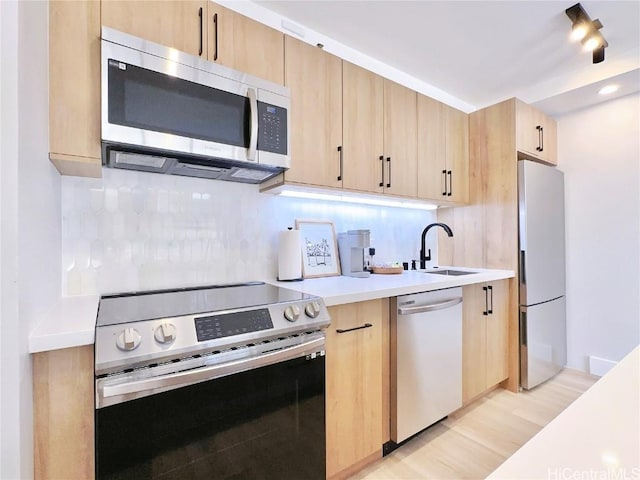 kitchen featuring stainless steel appliances, a sink, light countertops, light brown cabinetry, and tasteful backsplash