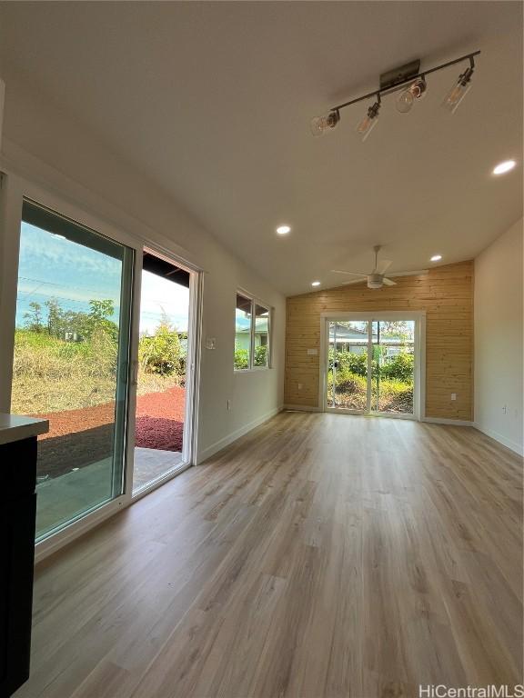 unfurnished living room featuring ceiling fan, wooden walls, a wealth of natural light, and light wood-type flooring