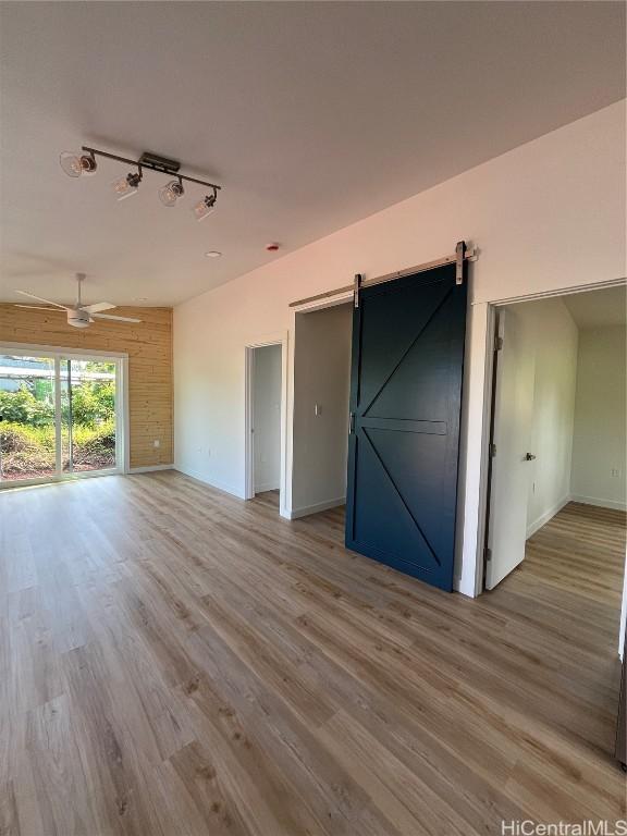 unfurnished room featuring track lighting, wooden walls, ceiling fan, a barn door, and hardwood / wood-style floors