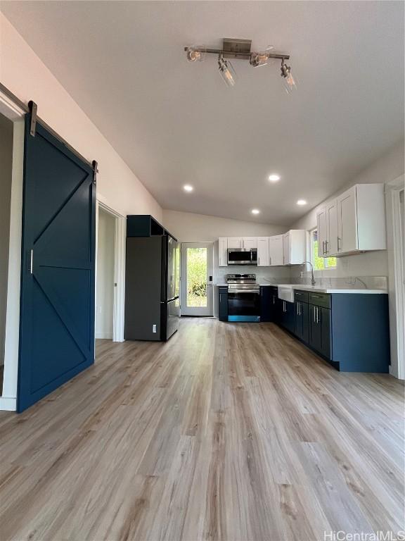 kitchen featuring white cabinetry, vaulted ceiling, light wood-type flooring, stainless steel appliances, and a barn door