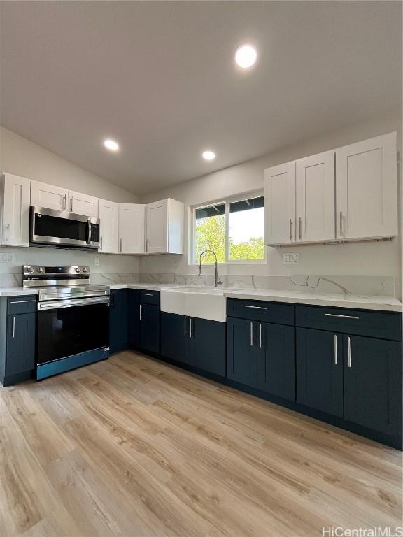 kitchen with stainless steel appliances, vaulted ceiling, white cabinets, and light hardwood / wood-style floors