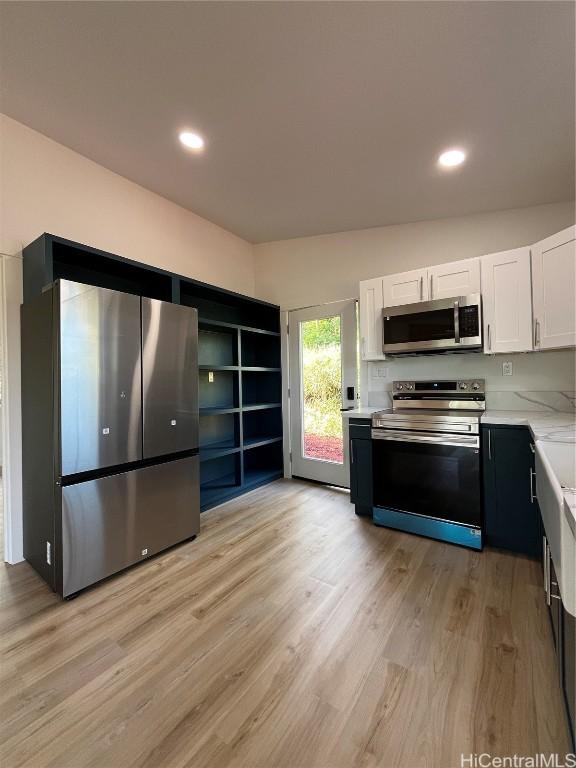 kitchen with appliances with stainless steel finishes, white cabinetry, lofted ceiling, light stone countertops, and light wood-type flooring