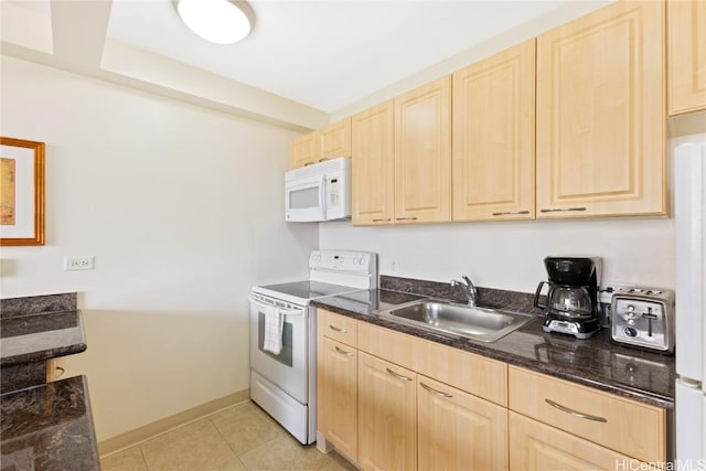 kitchen featuring white appliances, dark stone counters, light brown cabinetry, and sink